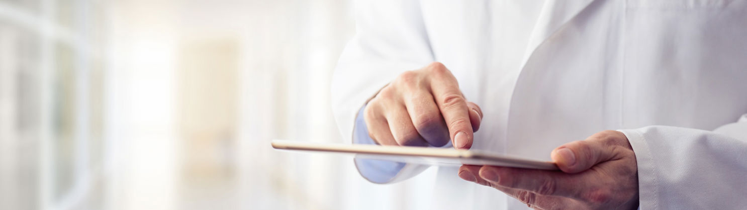 Arzt in weißem Kittel bedient Tablet in hellem Krankenhausflur