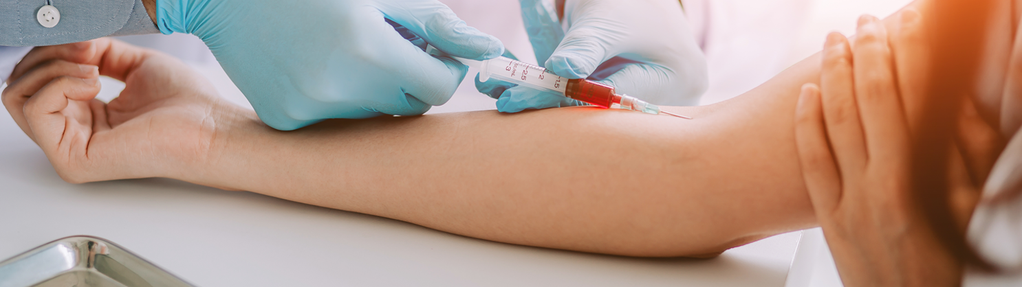 Arzt mit Handschuhen entnimmt mit einer Spritze Blut aus dem Arm einer sitzenden Person 